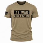 A short-sleeve crewneck t-shirt in heathered tan/khaki, featuring a distressed black graphic on the chest that reads 'AT WAR WITH MYSELF' in beige block letters. A black American flag graphic is printed on the right sleeve.