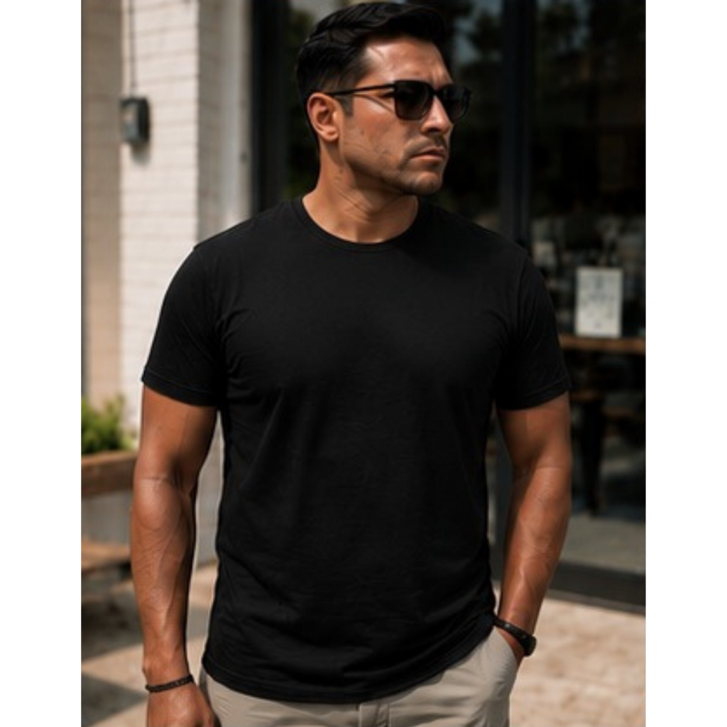 A man wearing a plain black short-sleeve crewneck t-shirt and beige pants, standing outdoors in front of a building with a glass storefront.