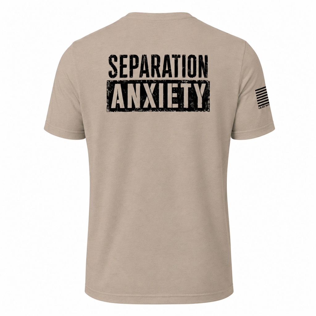 A light tan short-sleeve t-shirt shown from the back, featuring the words 'SEPARATION ANXIETY' printed in a distressed black block font across the upper back. A small black American flag graphic is printed on the left sleeve.
