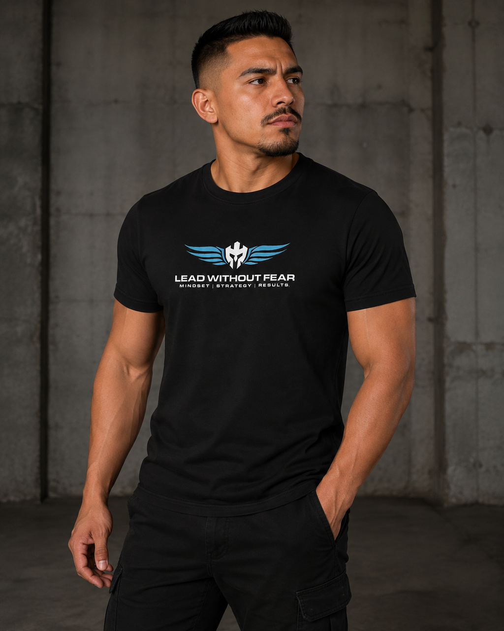 A muscular man wearing a black crewneck t-shirt with a blue and white winged logo and the text 'LEAD WITHOUT FEAR' on the chest, standing against a dark concrete wall.