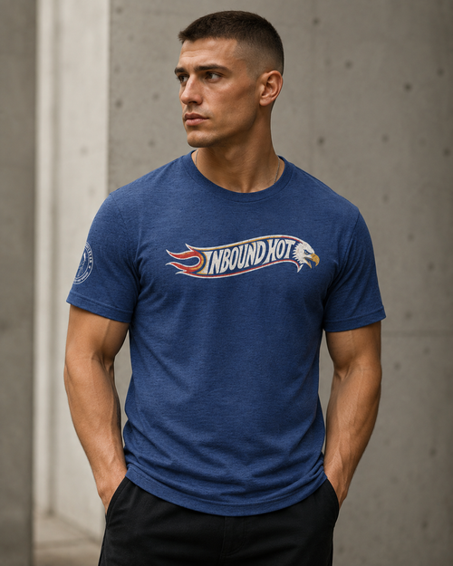 A man wearing a heather blue crewneck t-shirt with a 'NBOUND HOT' graphic across the chest, standing against a concrete wall.
