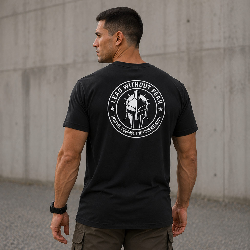 A man wearing a black t-shirt with a white circular graphic on the back, standing outdoors against a concrete wall.