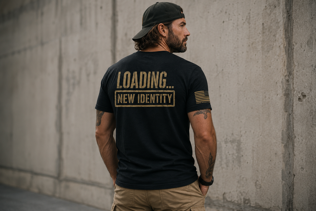 A man wearing a black t-shirt with 'LOADING... NEW IDENTITY' printed in gold on the back, standing against a concrete wall.