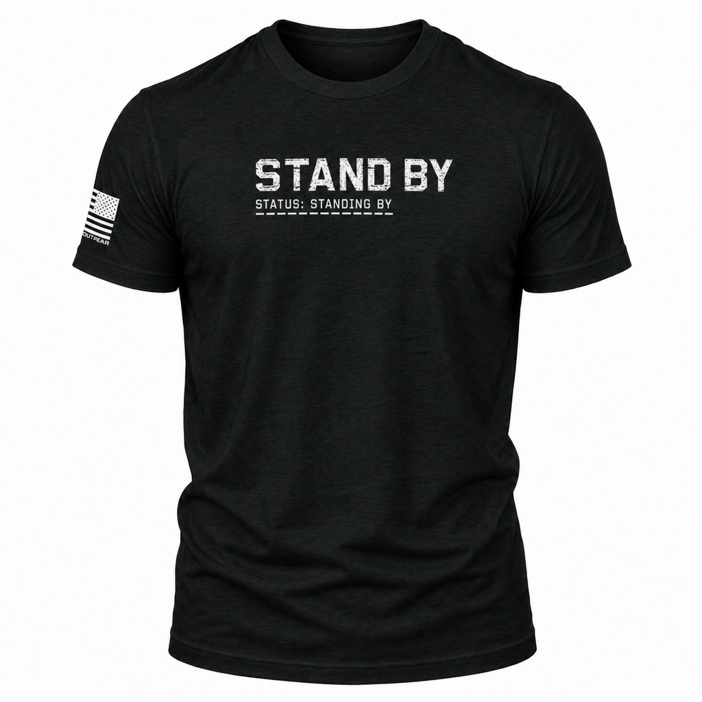 A black short-sleeve t-shirt with 'STAND BY' printed in distressed white letters on the chest, with 'STATUS: STANDING BY' underneath. A distressed black-and-white American flag is printed on the right sleeve.