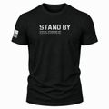 A black short-sleeve t-shirt with 'STAND BY' printed in distressed white letters on the chest, with 'STATUS: STANDING BY' underneath. A distressed black-and-white American flag is printed on the right sleeve.