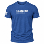 A heather blue short-sleeve t-shirt with 'STAND BY' printed in distressed white letters on the chest, with smaller text underneath and a distressed American flag graphic on the right sleeve, shown on a plain white background.