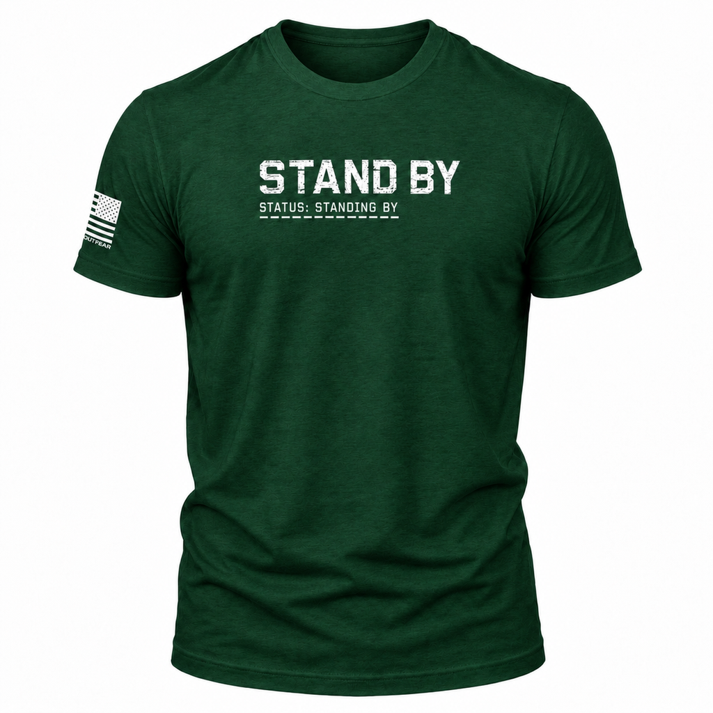 A dark green heathered short-sleeve t-shirt with 'STAND BY' and 'STATUS: STANDING BY' printed in distressed white text on the chest, featuring a black-and-white American flag graphic on the right sleeve, shown on a plain white background.