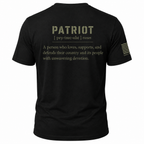 Black short-sleeve t-shirt shown from the back, featuring a printed dictionary-style definition of the word 'Patriot' in olive drab and white text, with a small American flag graphic and 'EST. 2021' on the sleeve.
