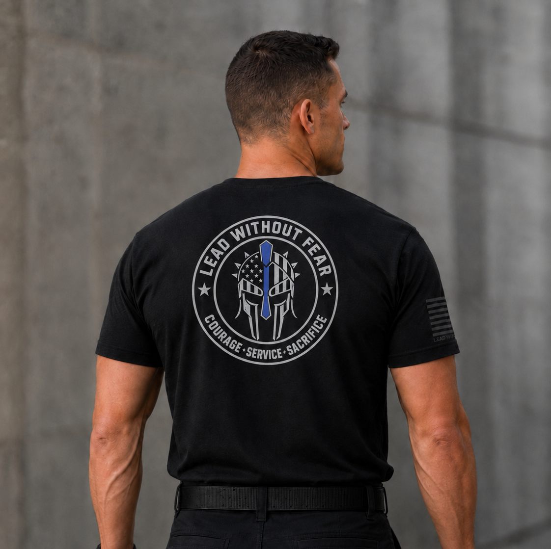 A man viewed from behind wearing a black short-sleeve tactical T-shirt with a large circular back graphic that reads 'LEAD WITHOUT FEAR' and 'COURAGE - SERVICE - SACRIFICE' around a police badge design. The shirt also has a small black flag-style print on the right sleeve.
